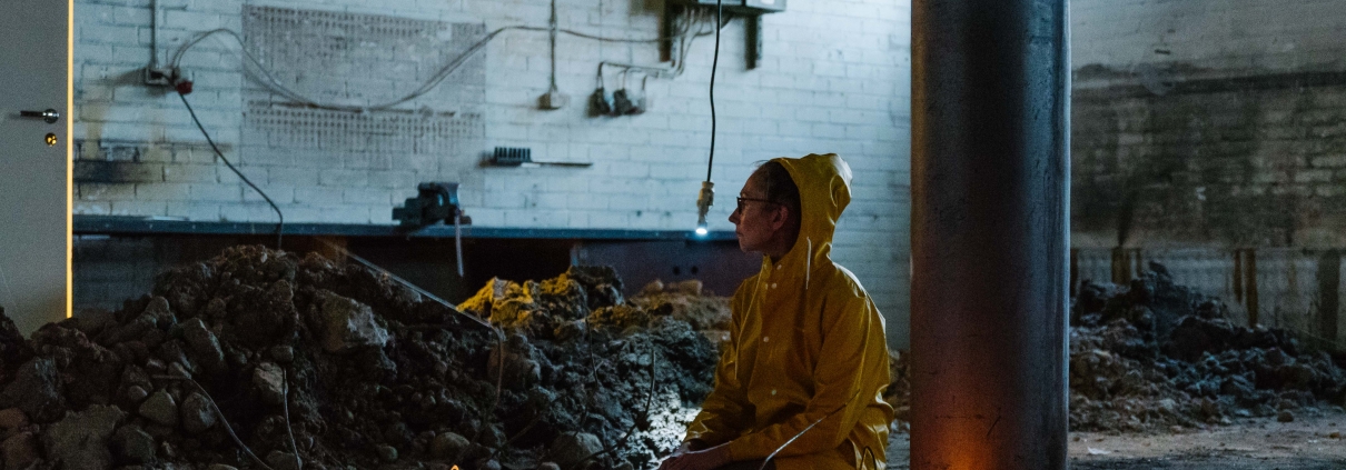 keltaiseen sadetakkiin pukeutunut hahmi istuu tyhjässä teollisuushallissa